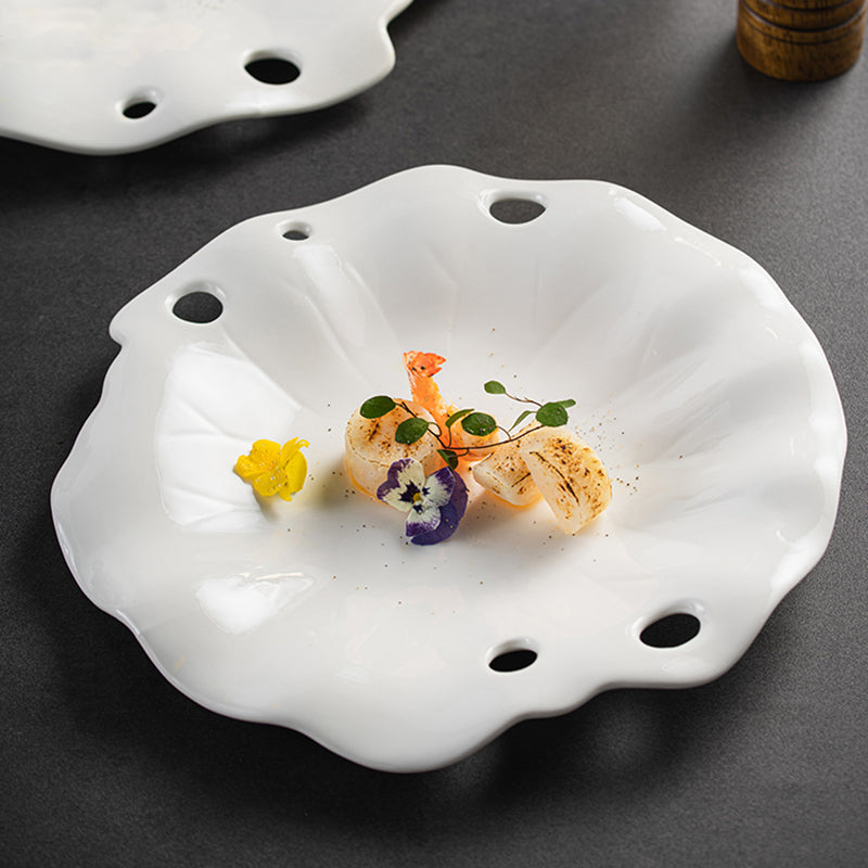 Unique white ceramic plate with irregular scalloped edges and artistic cutout holes, ideal for modern gourmet plating and fine dining presentations